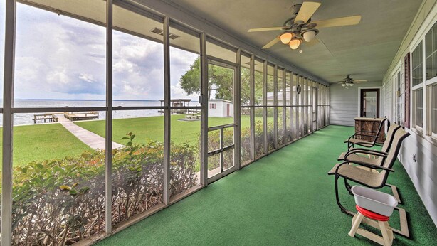 A covered porch with a view of the ocean, green artificial turf, and outdoor furniture. - Lakefront Livingston Home w/ Dock, 1 Mi to Launch! (Livingston)