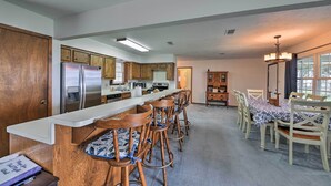 A modern kitchen with a central island, wooden bar stools, and a dining table with chairs. - Lakefront Livingston Home w/ Dock, 1 Mi to Launch! (Livingston)