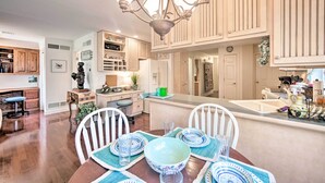 A spacious kitchen with wooden cabinets, a central island, and a dining area with white chairs and blue and white plates. - 9 Mi to Midtown Harrisburg: Cottage w/ Deck (Harrisburg)