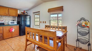 A kitchen with wooden cabinets, a black refrigerator, a microwave, a wooden dining table with chairs, a window with a view of the landscape, and a decorative metal rack on the wall. - Charming Santa Rosa Home w/ Mountain Views & Porch (Santa Rosa)