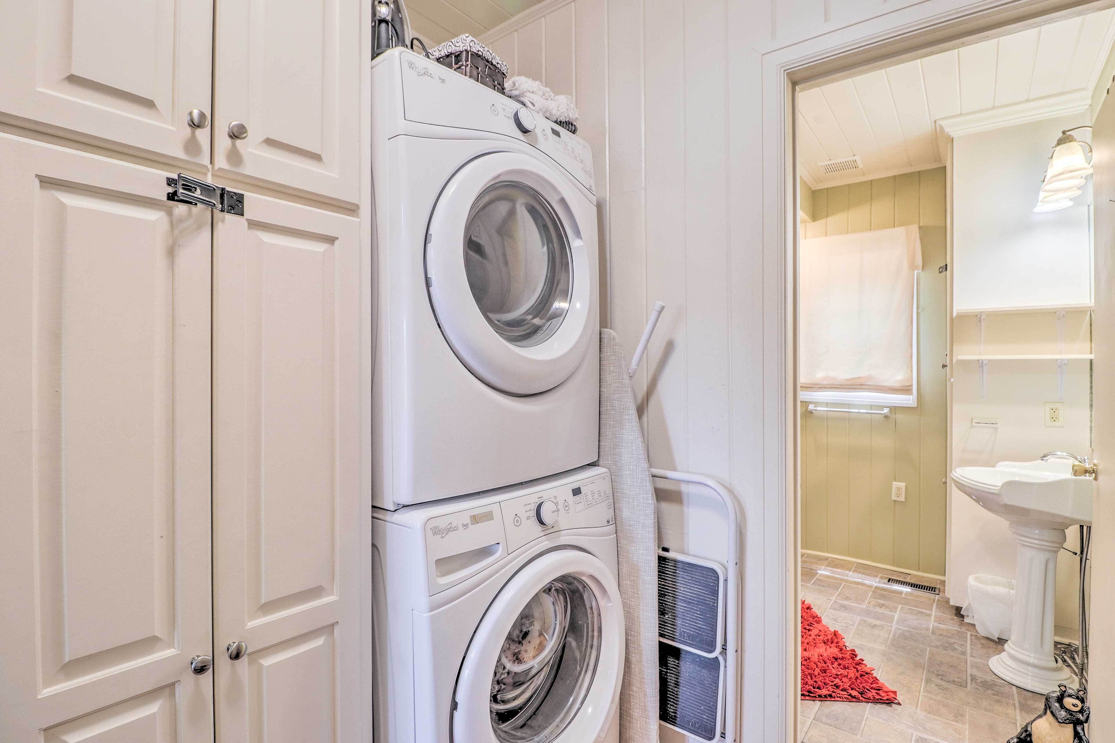 A laundry area with stacked washing machines, a red rug, and a bathroom with a pedestal sink and toilet.