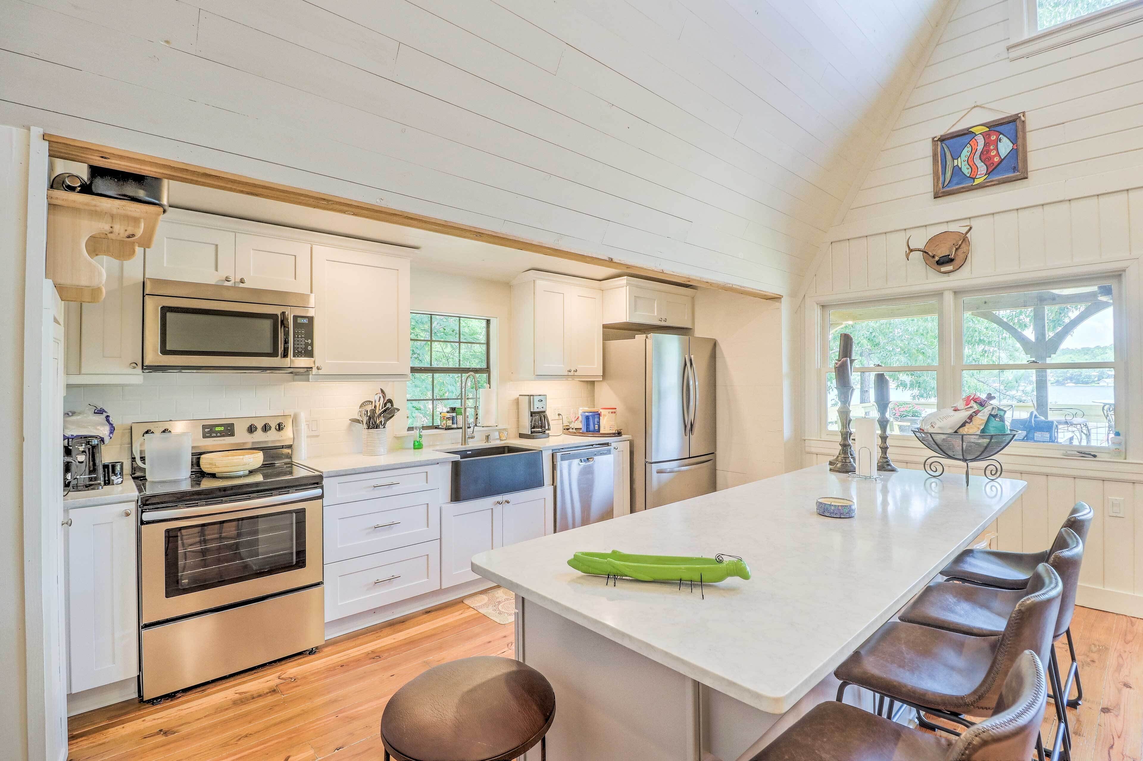 A kitchen with white cabinets, stainless steel appliances, a large island with bar stools, and a view through the window.