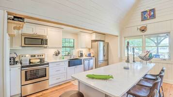 A kitchen with white cabinets, stainless steel appliances, a large island with bar stools, and a view through the window.