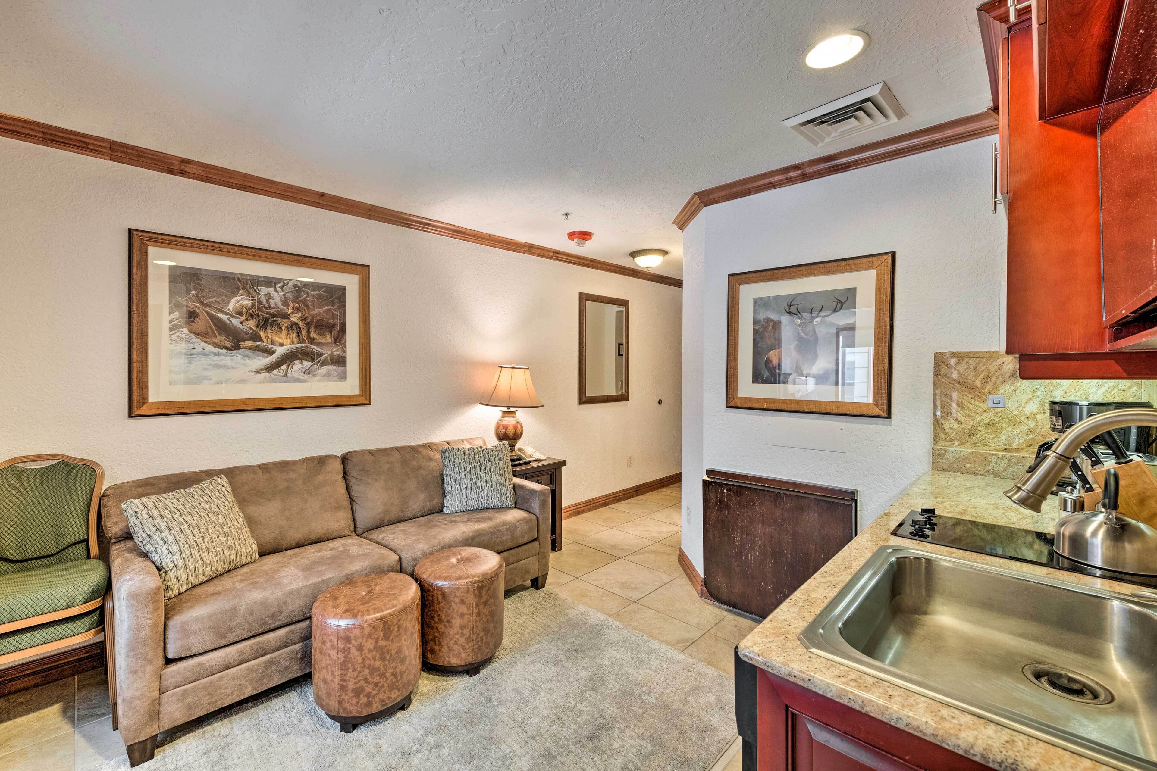 A living room with a brown sofa, two ottomans, a lamp, and framed artwork on the walls.