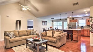 A spacious living room with a large brown sectional sofa, a coffee table with flowers, and a dining area with a wooden table and chairs.