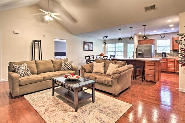 A spacious living room with a large brown sectional sofa, a coffee table with flowers, and a dining area with a wooden table and chairs. - 2 Bed Home, Garage, Seasonal Pool, Island 2 Miles! (Pigeon Forge)