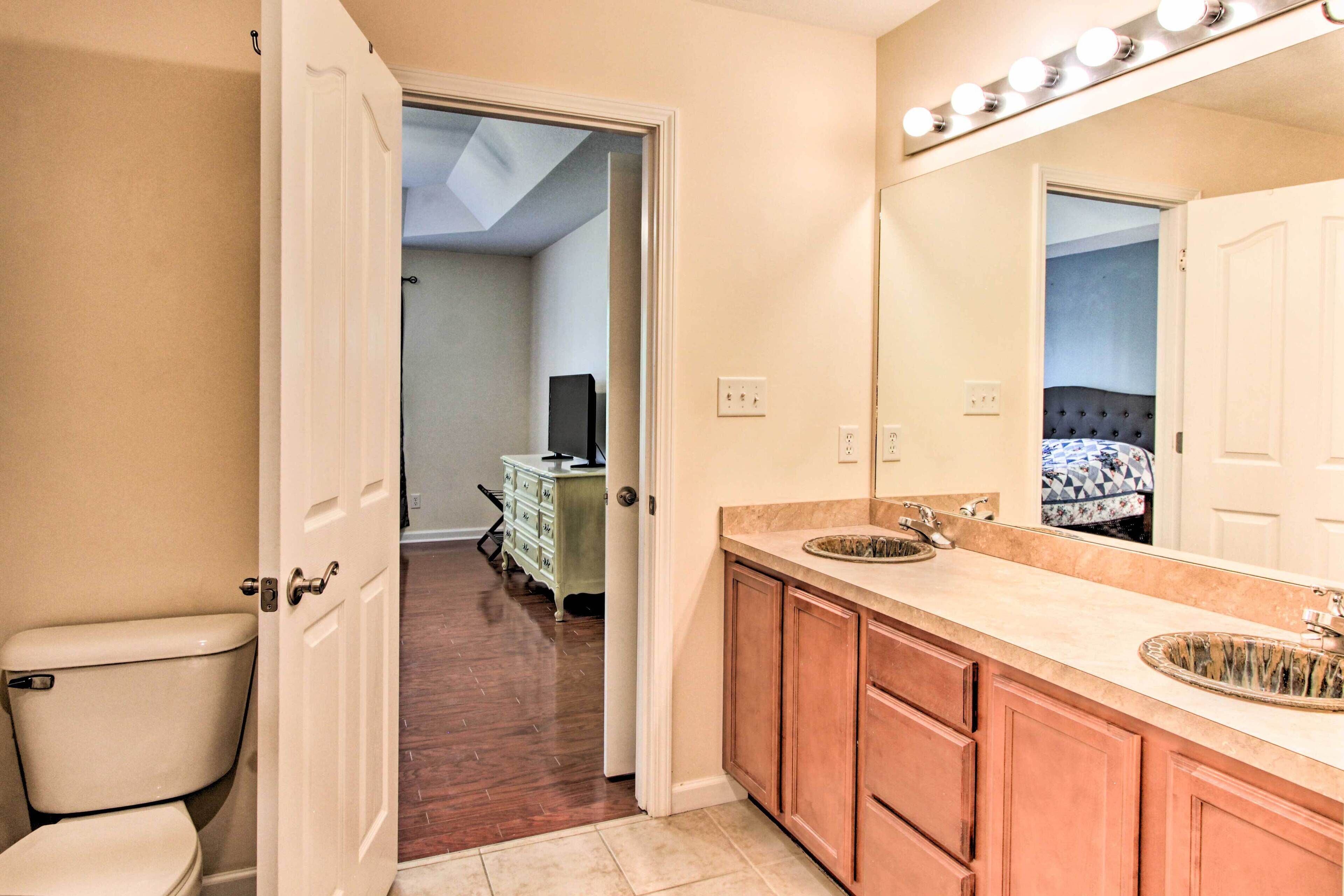 A bathroom with a toilet, sink, mirror, and vanity. There is a door leading to another room.
