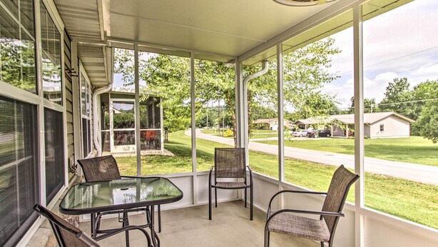 A covered patio with a glass table and chairs, large windows, and a view of a residential street and greenery.