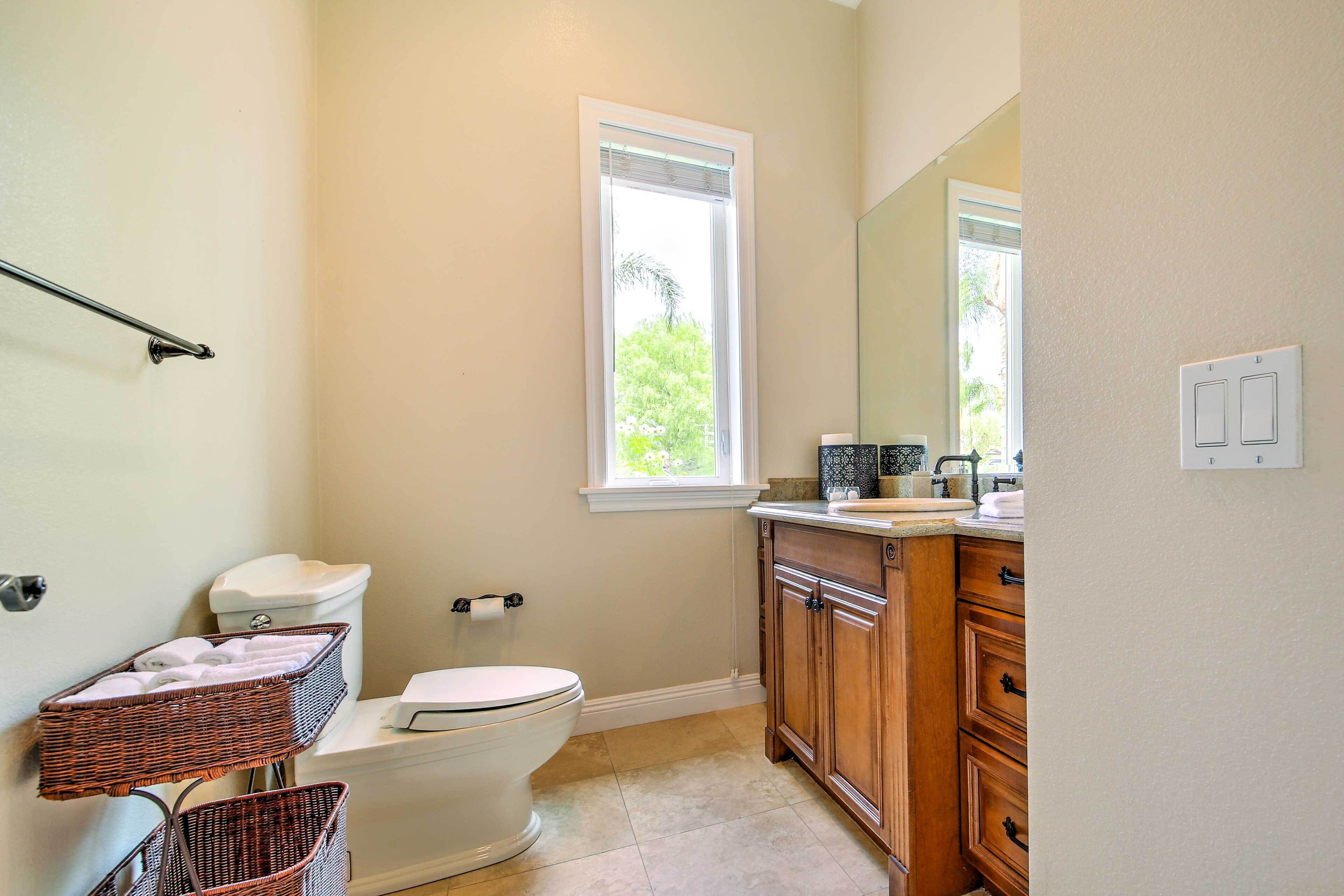 A bathroom with a toilet, wicker baskets, a window, and wooden cabinets.