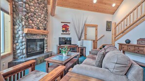 A cozy living room with a stone fireplace, wooden furniture, and a staircase.