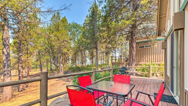 A wooden deck with red chairs and a table, overlooking a forested area.