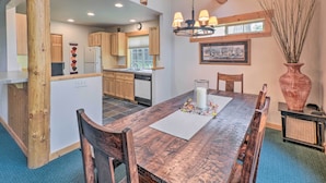 A modern kitchen with wooden cabinets, a dining area with a wooden table, and a rustic ceiling.