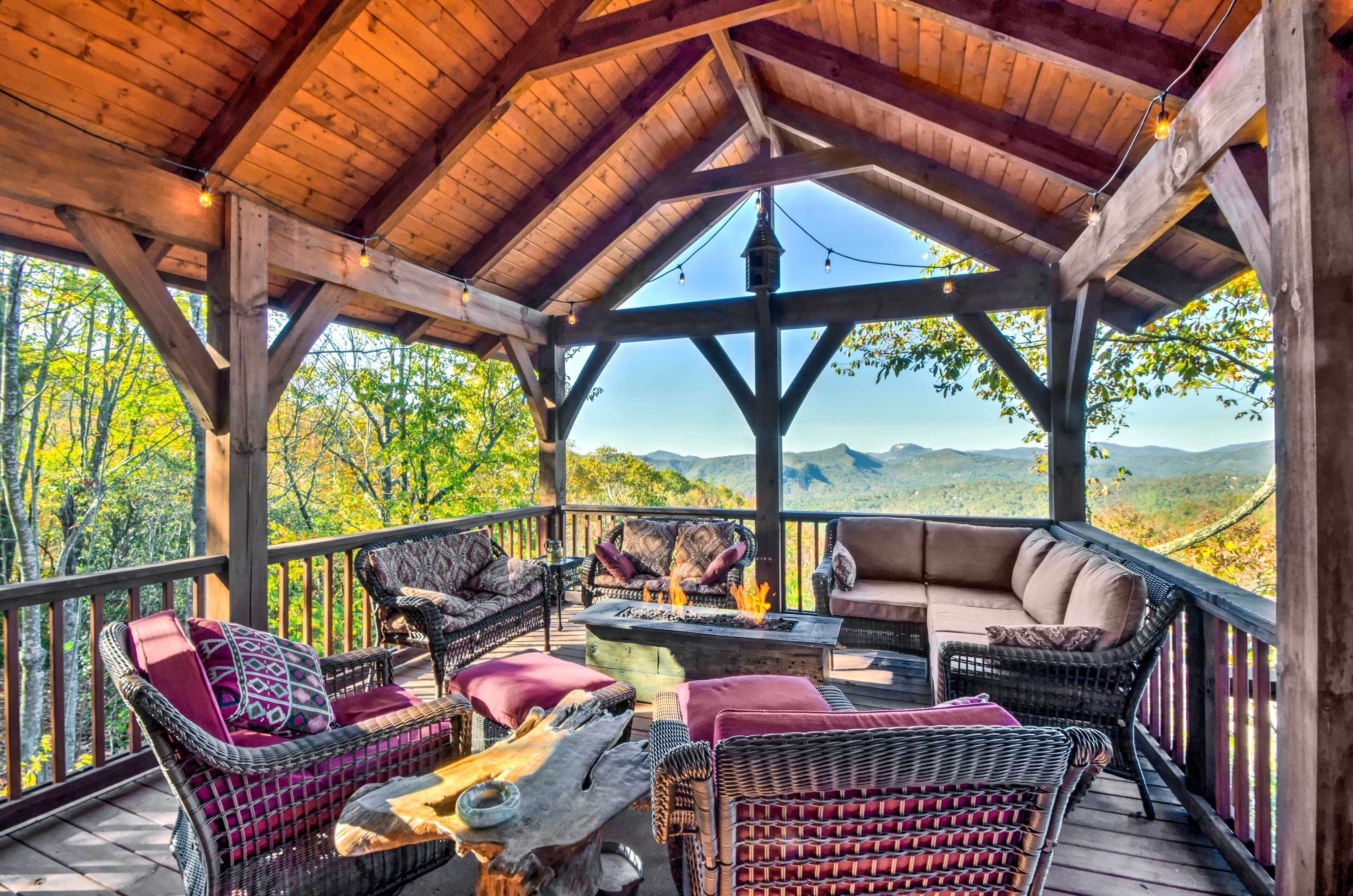 An outdoor covered patio with wicker furniture, a fire pit, and a view of the surrounding landscape.
