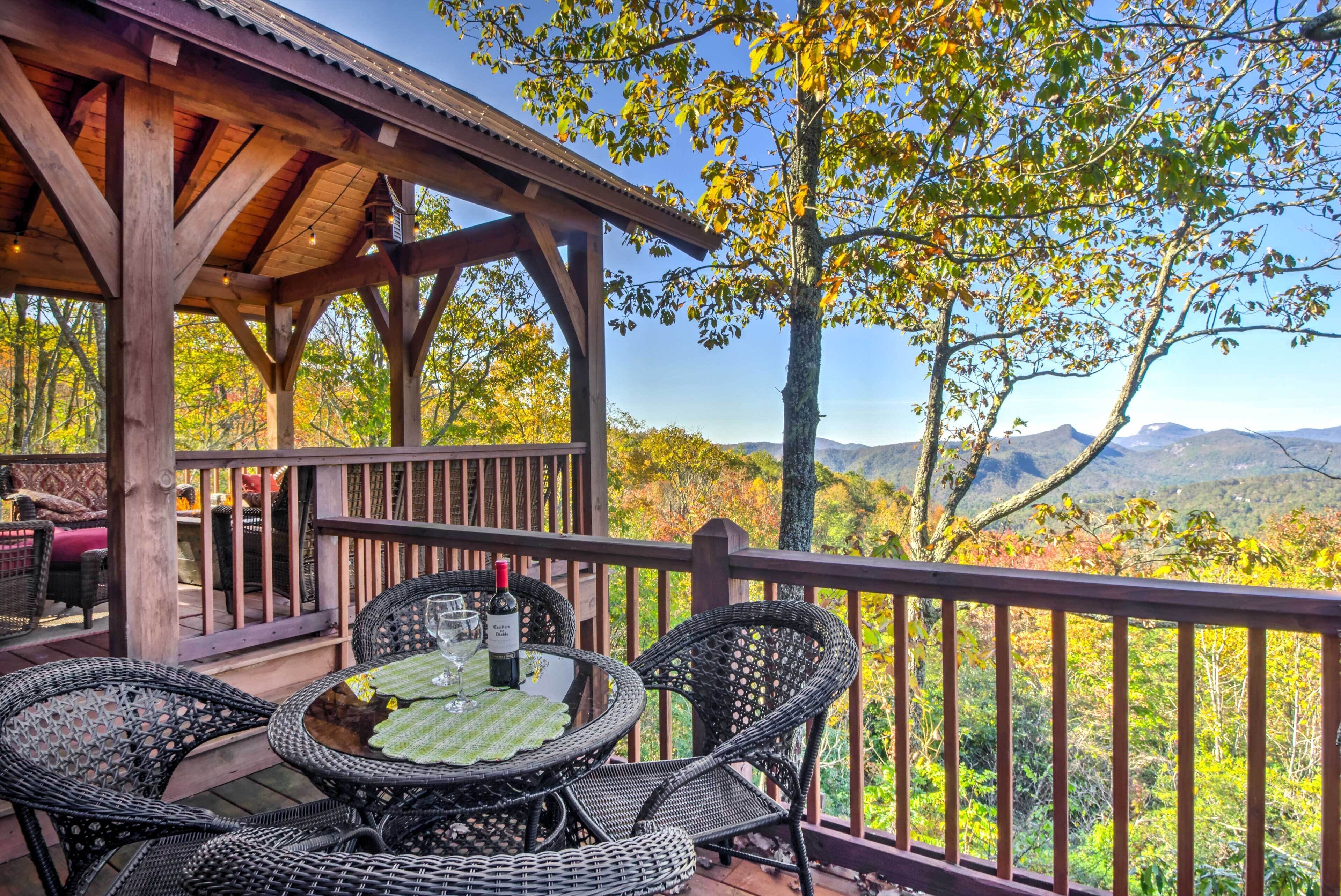 A wooden deck with wicker chairs and a table set for dining, overlooking a mountainous landscape.