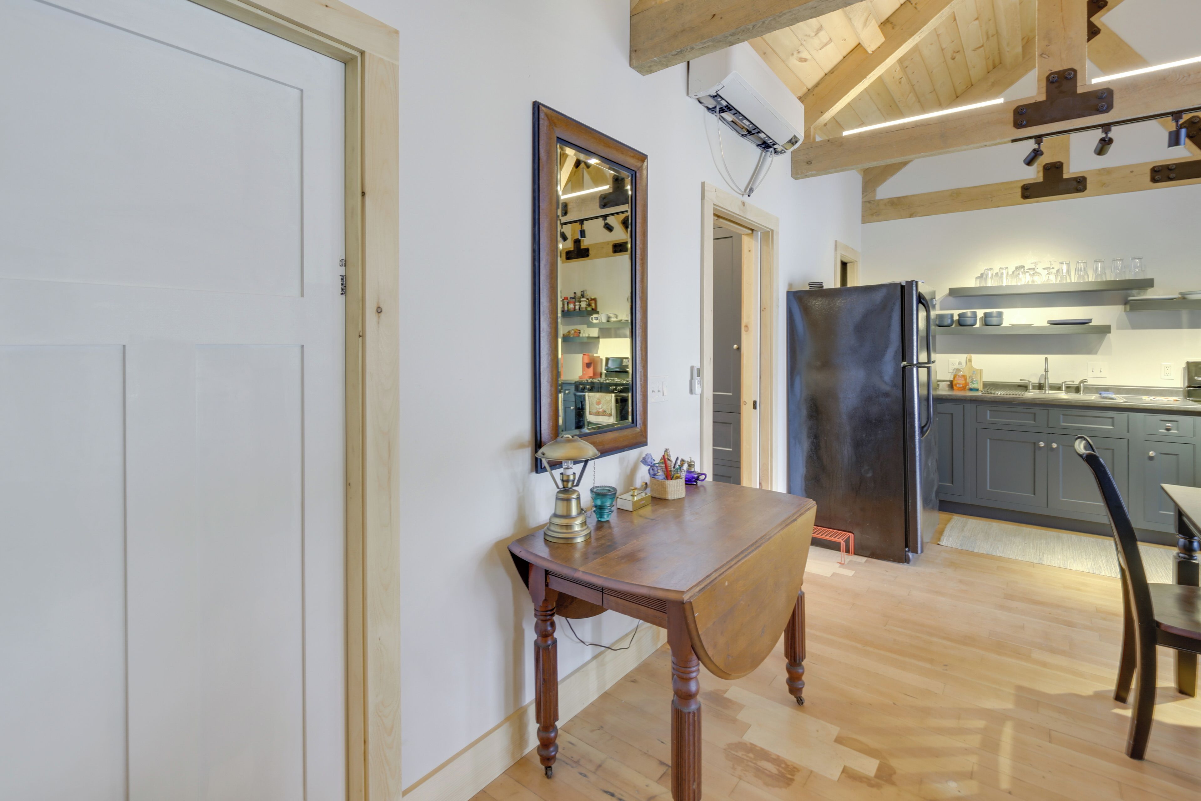Un coin repas avec une table en bois, un miroir et une cuisine en arrière-plan.