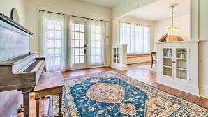Una habitación espaciosa con un piano de cola, un tapete grande y ornamentado, y un aparador con puertas de cristal.