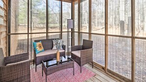 Un espacio de estar cubierto al aire libre con mobiliario de mimbre, una mesa de vidrio y vistas a un bosque.