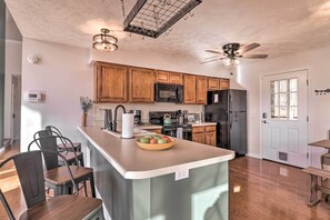 A modern kitchen with wooden cabinets, stainless steel appliances, and a central island with a bowl of fruit.