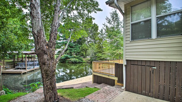A house with a dock extending into a calm pond, surrounded by lush greenery.