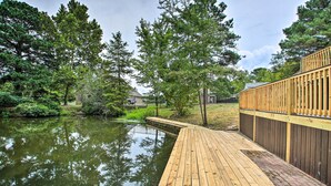 A wooden deck extending over a calm body of water, surrounded by lush greenery and trees.