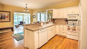 A kitchen with white cabinets, a microwave, and a refrigerator. There is a wooden floor and a rug in the living area.