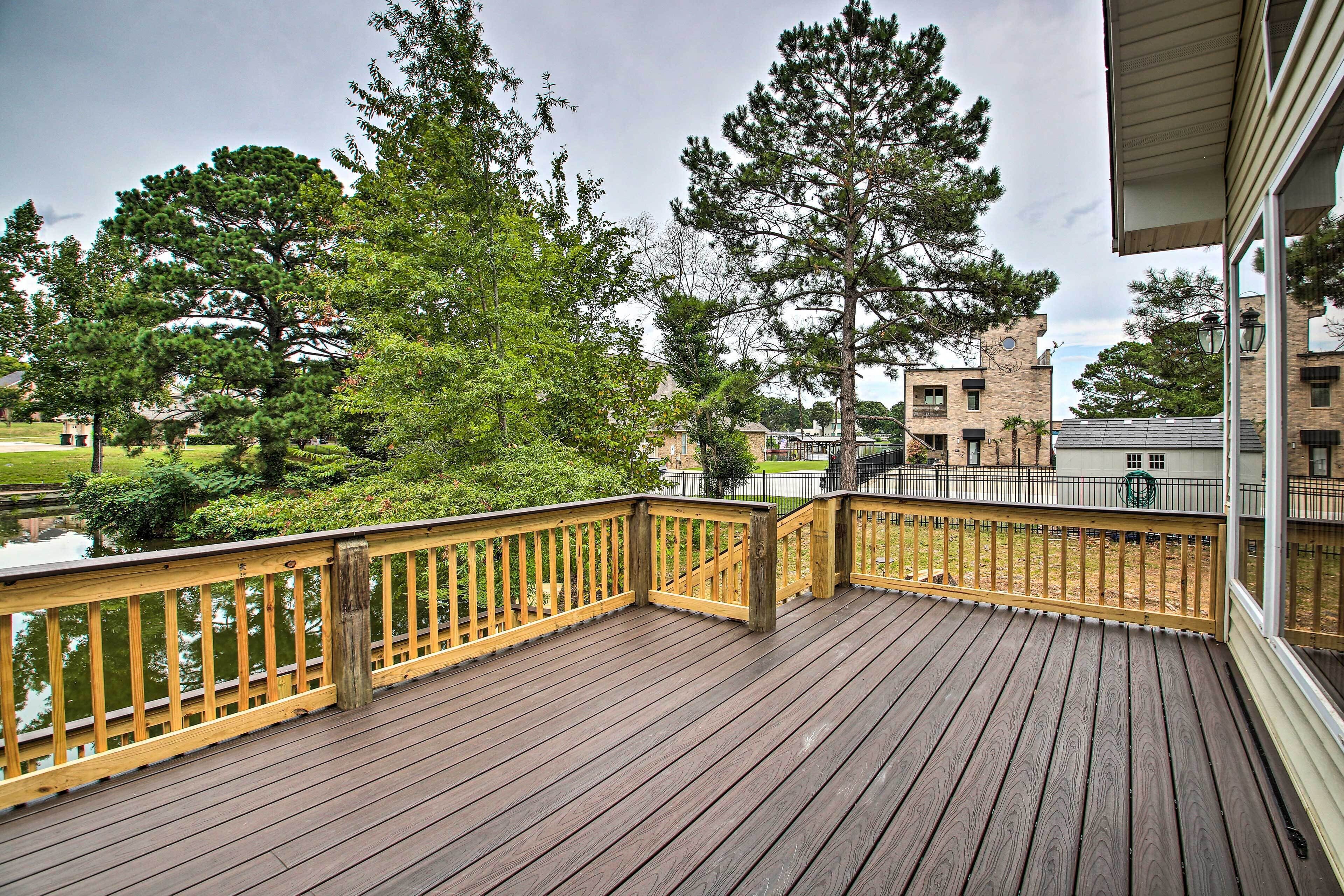 A wooden deck with a railing, overlooking a landscaped area with trees and a building in the background.