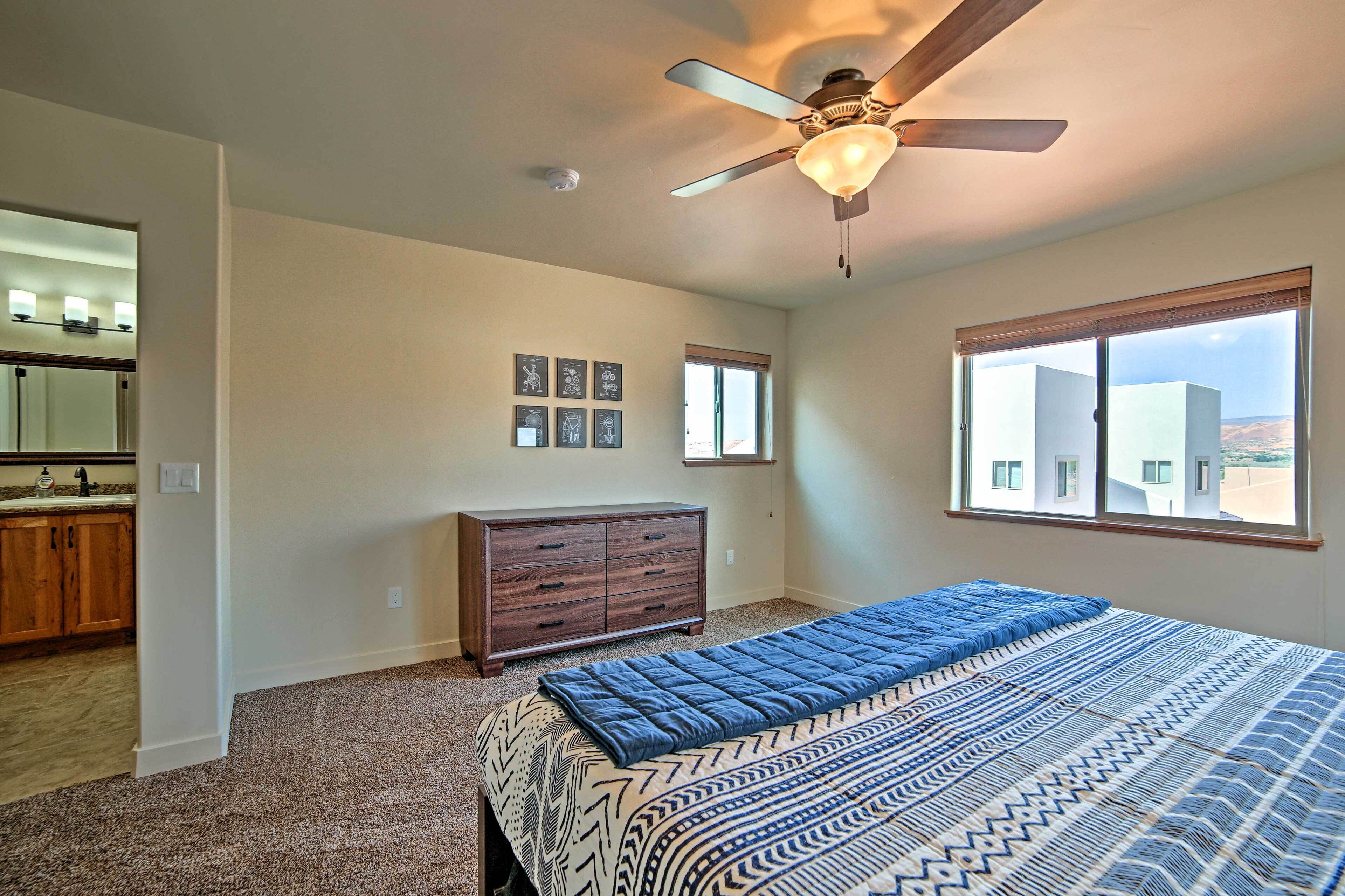 A bedroom with a bed, dresser, ceiling fan, and a window with a view.