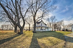 A large, single-story house with a porch, surrounded by trees and a well-maintained lawn.