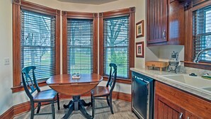 A corner dining area with a wooden table and chairs, large windows with blinds, and a kitchen with wooden cabinets and a dishwasher. - Lawrence Area Vacation Rental 15 Mi to Topeka! (Lecompton)