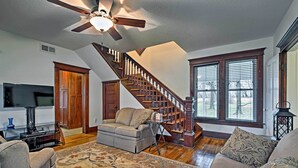 A living room with a sofa, a coffee table, a TV, a fireplace, and a staircase. - Lawrence Area Vacation Rental 15 Mi to Topeka! (Lecompton)
