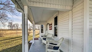 A porch with two rocking chairs and a flag on the wall. - Lawrence Area Vacation Rental 15 Mi to Topeka! (Lecompton)