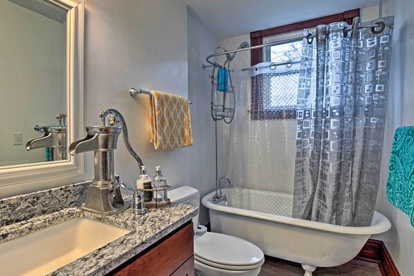 A bathroom with a granite countertop sink, a white toilet, a white bathtub, and a shower with a glass door.
