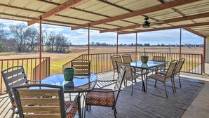 An outdoor patio with a table and chairs, a ceiling fan, and a view of a rural landscape.