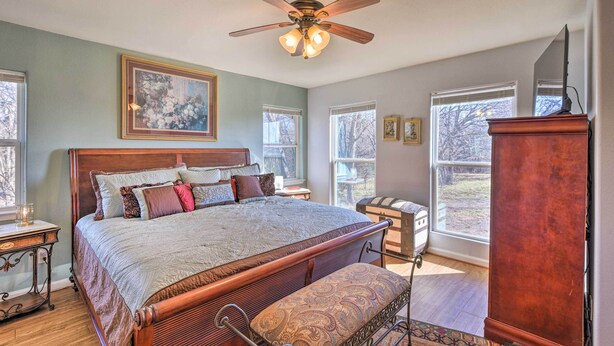 A bedroom with a large bed, a ceiling fan, and multiple windows.