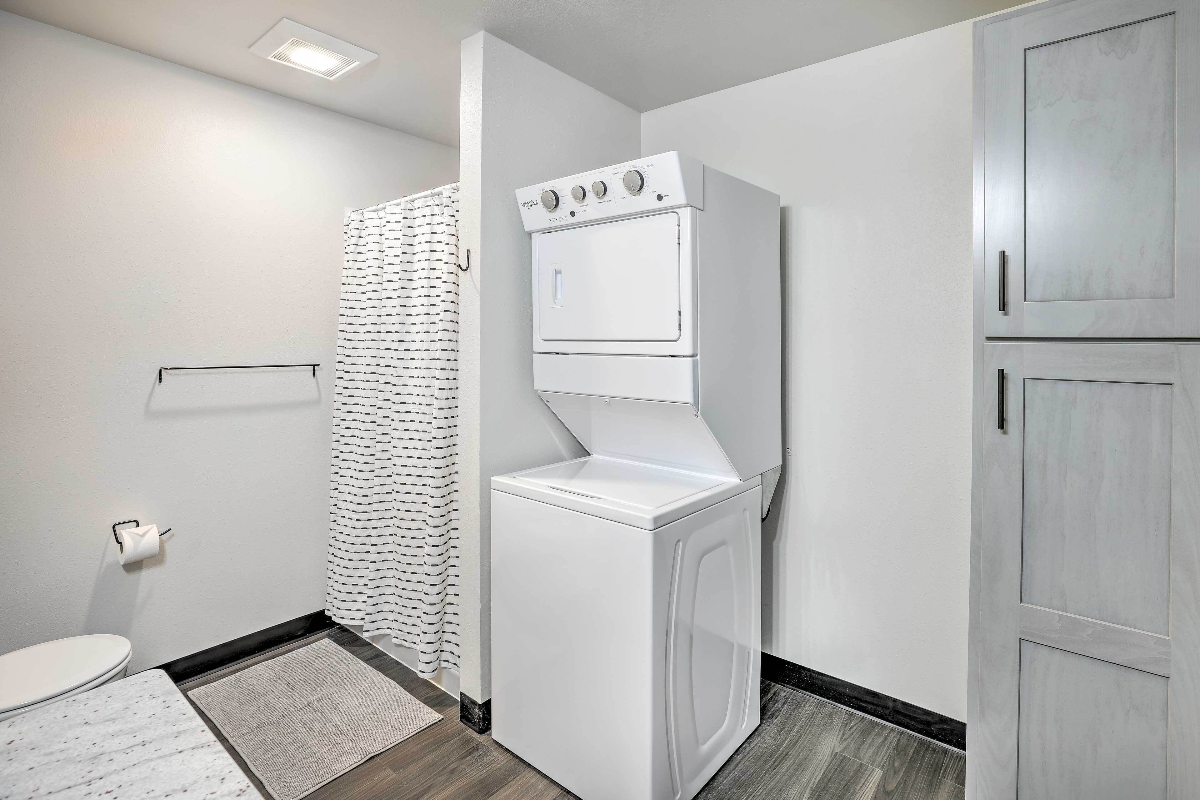 A laundry room with a front-loading washer and dryer, a towel rack, and a shower curtain.
