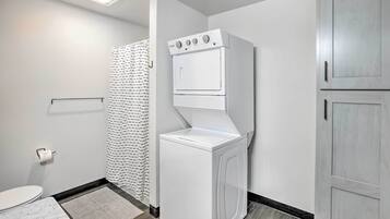 A laundry room with a front-loading washer and dryer, a towel rack, and a shower curtain.
