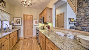 A kitchen with wooden cabinets, granite countertops, a stone fireplace, and a chandelier. - Beautiful Lake Glenville Townhome w/ Mountain View (Cashiers)