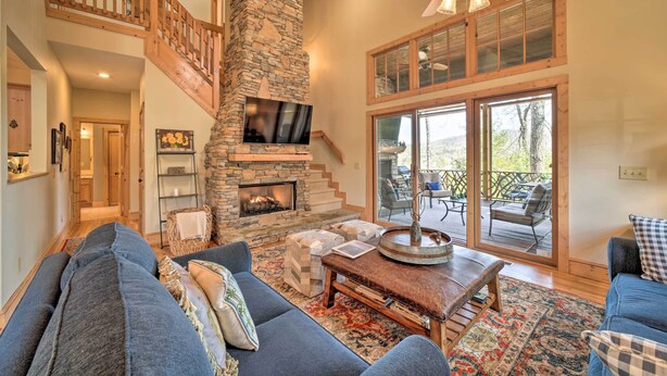 A spacious living room with a stone fireplace, a large sofa, and a dining area. - Beautiful Lake Glenville Townhome w/ Mountain View (Cashiers)
