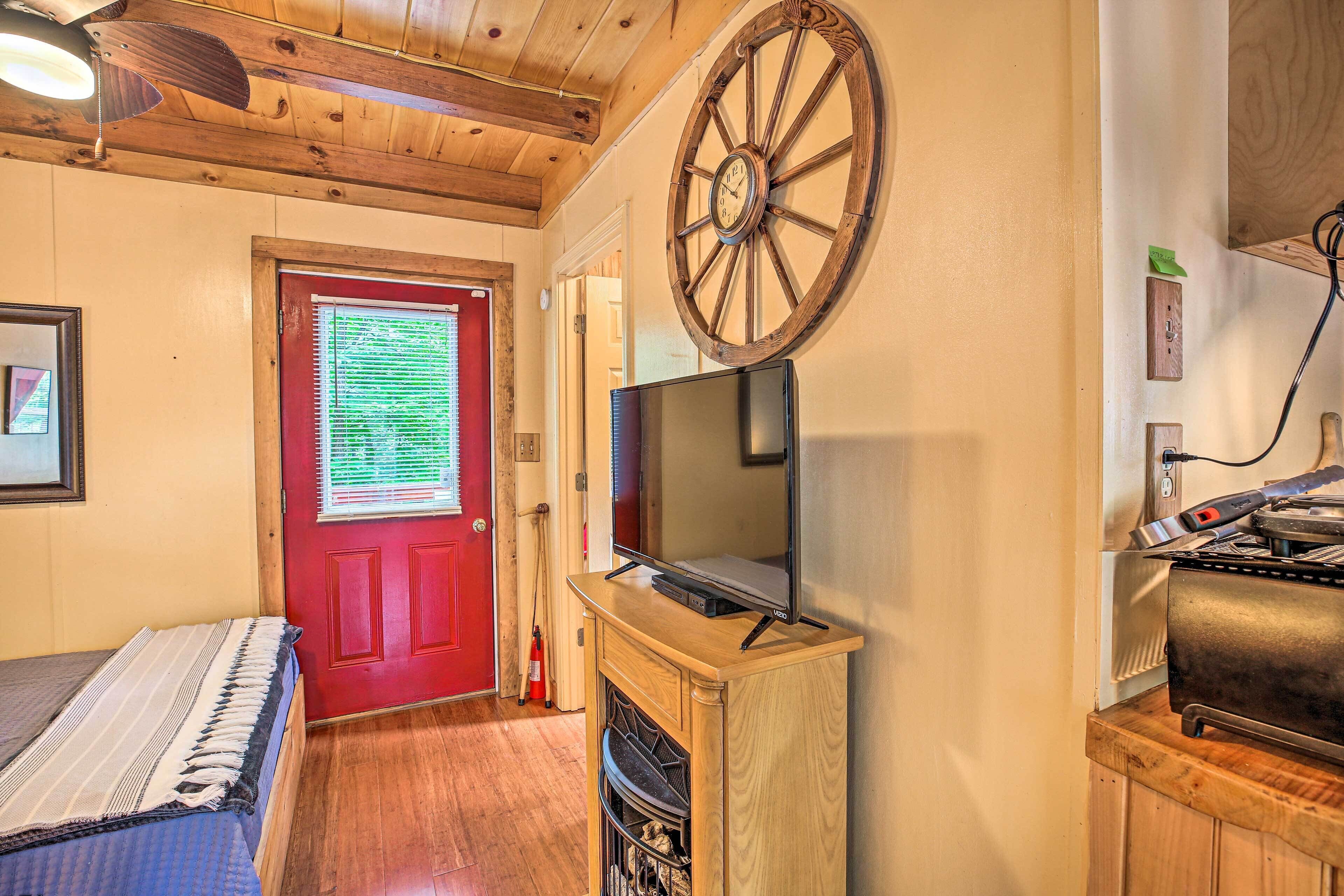 A room with a wooden ceiling, a red door, a television on a wooden stand, and a fireplace.