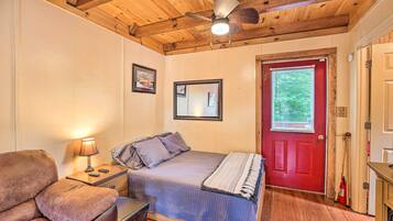 A bedroom with a bed, a nightstand, a lamp, a wooden ceiling, a red door, and a window with blinds.