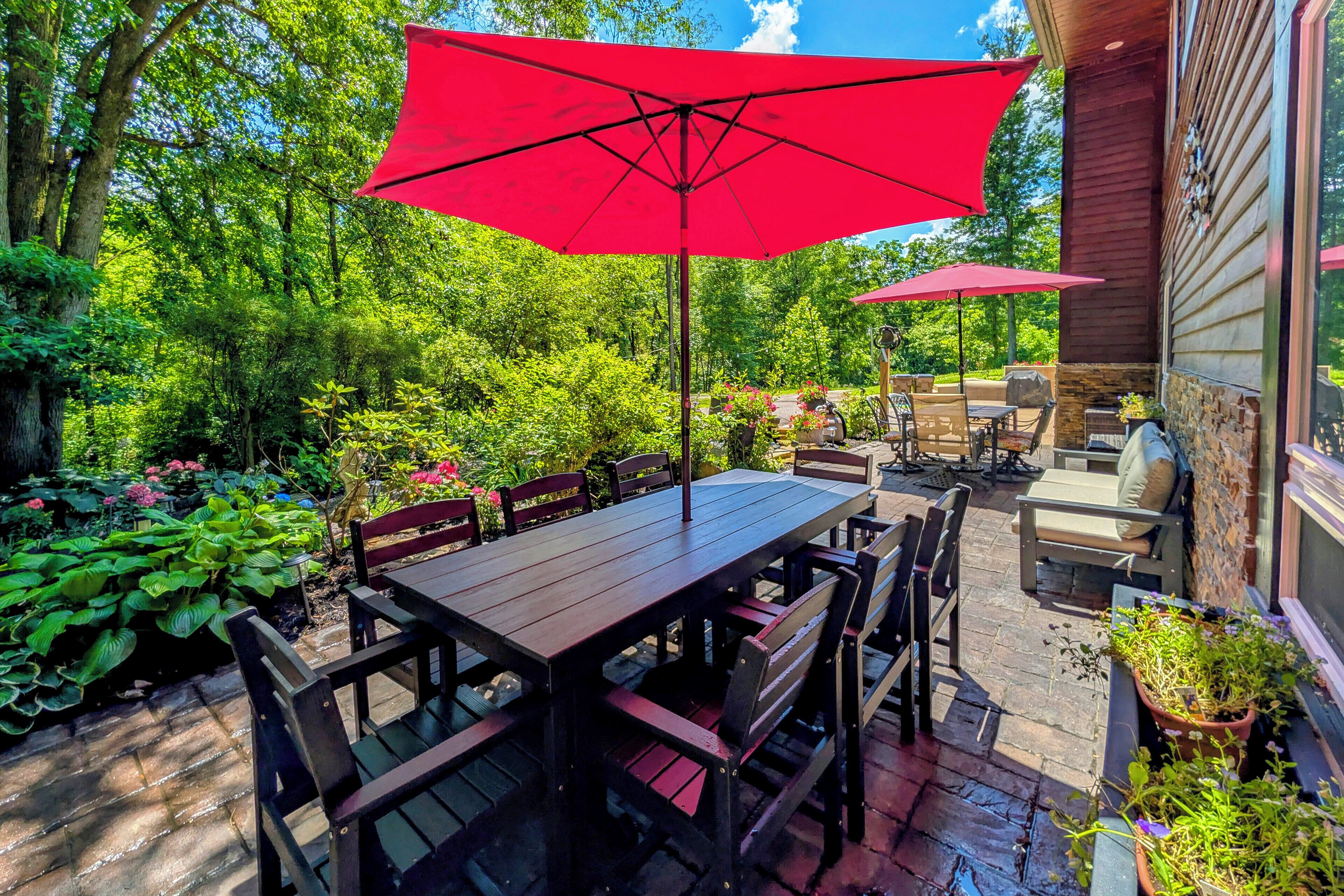 An outdoor patio with a wooden table and chairs, red umbrellas, and potted plants.