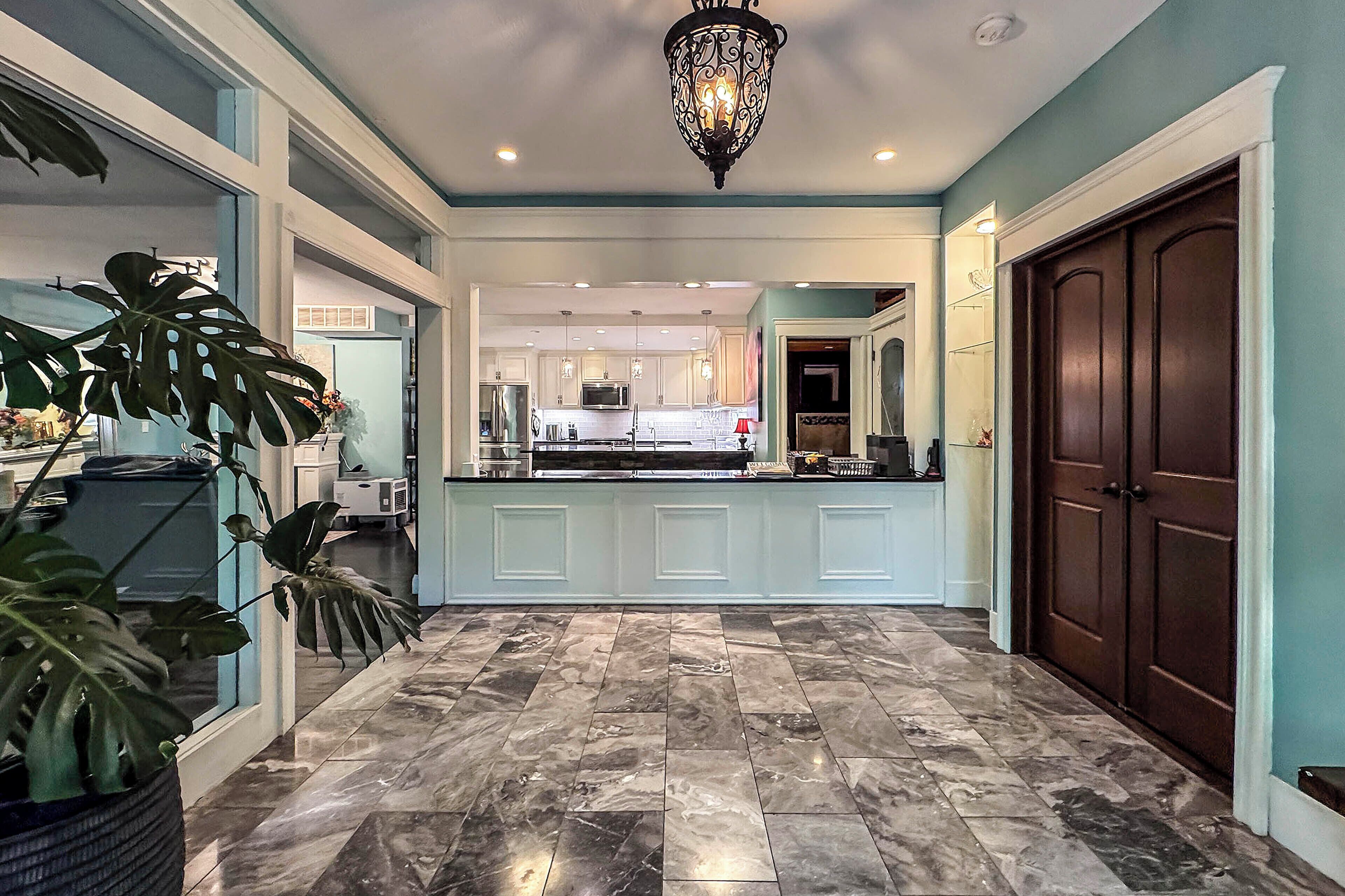 A spacious kitchen with white cabinetry, a marble floor, and a large window.