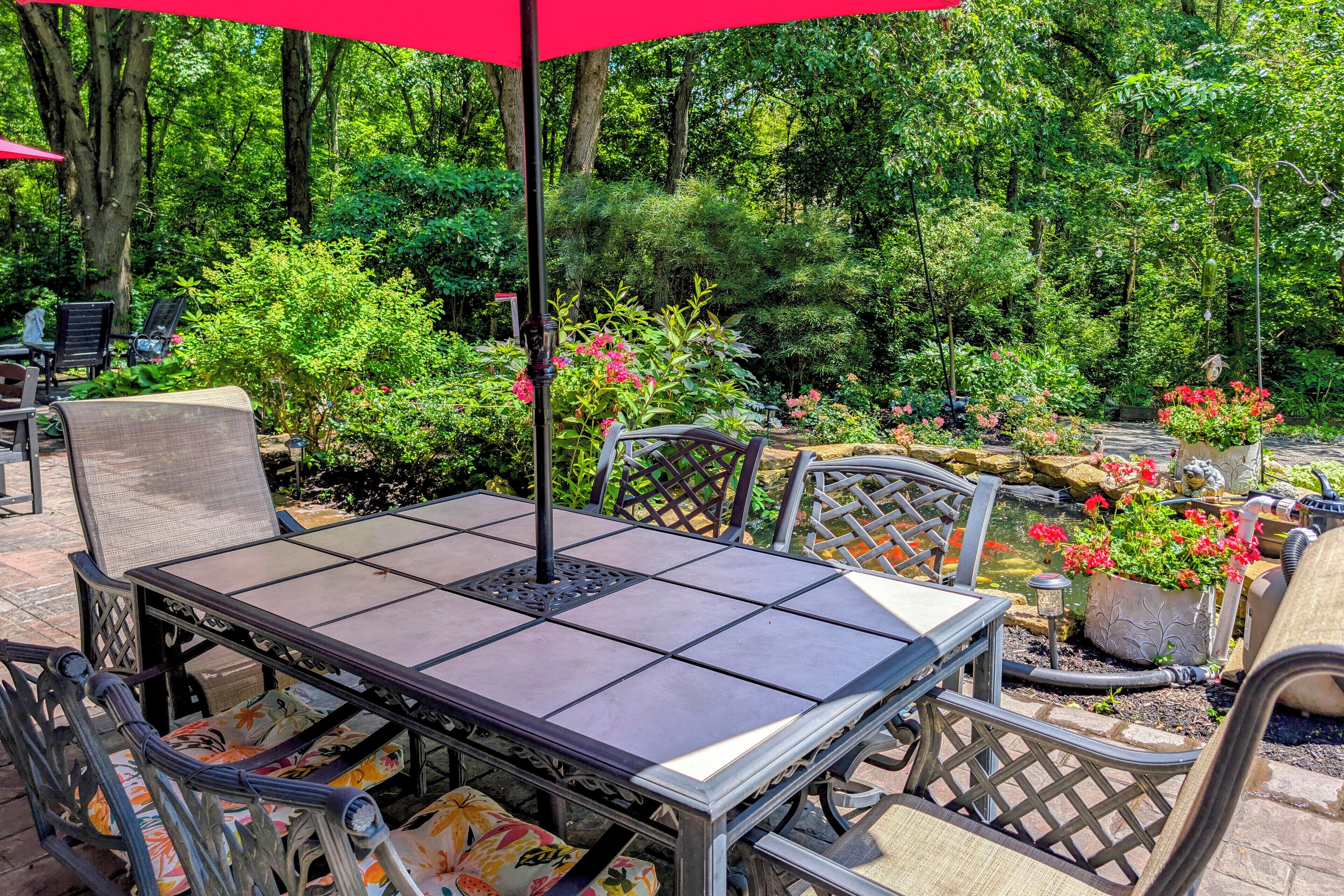 An outdoor patio with a table and chairs, surrounded by lush greenery and a small pond.
