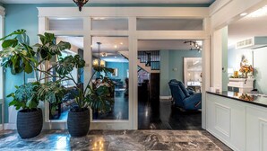 A spacious interior with a marble floor, large potted plants, a blue chair, and a kitchen area. - Woodland Spa Sanctuary: Delaware Home w/ Swim Spa (Delaware)