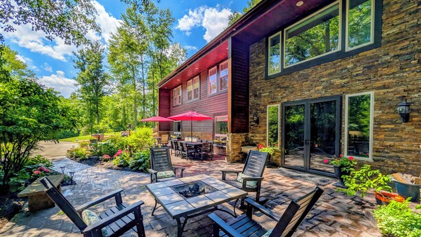 A patio with outdoor furniture, a fire pit, and a stone wall. - Woodland Spa Sanctuary: Delaware Home w/ Swim Spa (Delaware)