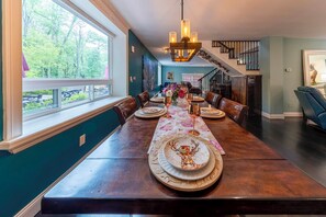 A dining area with a long table set for six, a chandelier, and a staircase leading to an upper level.
