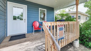 Une véranda avec une terrasse en bois, une chaise rouge et une porte blanche.