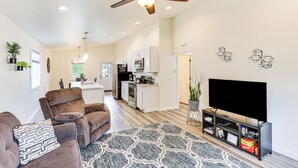 Un salon moderne avec un canapé en cuir marron, un tapis à motifs, un ventilateur de plafond et un téléviseur à écran plat posé sur un meuble noir.