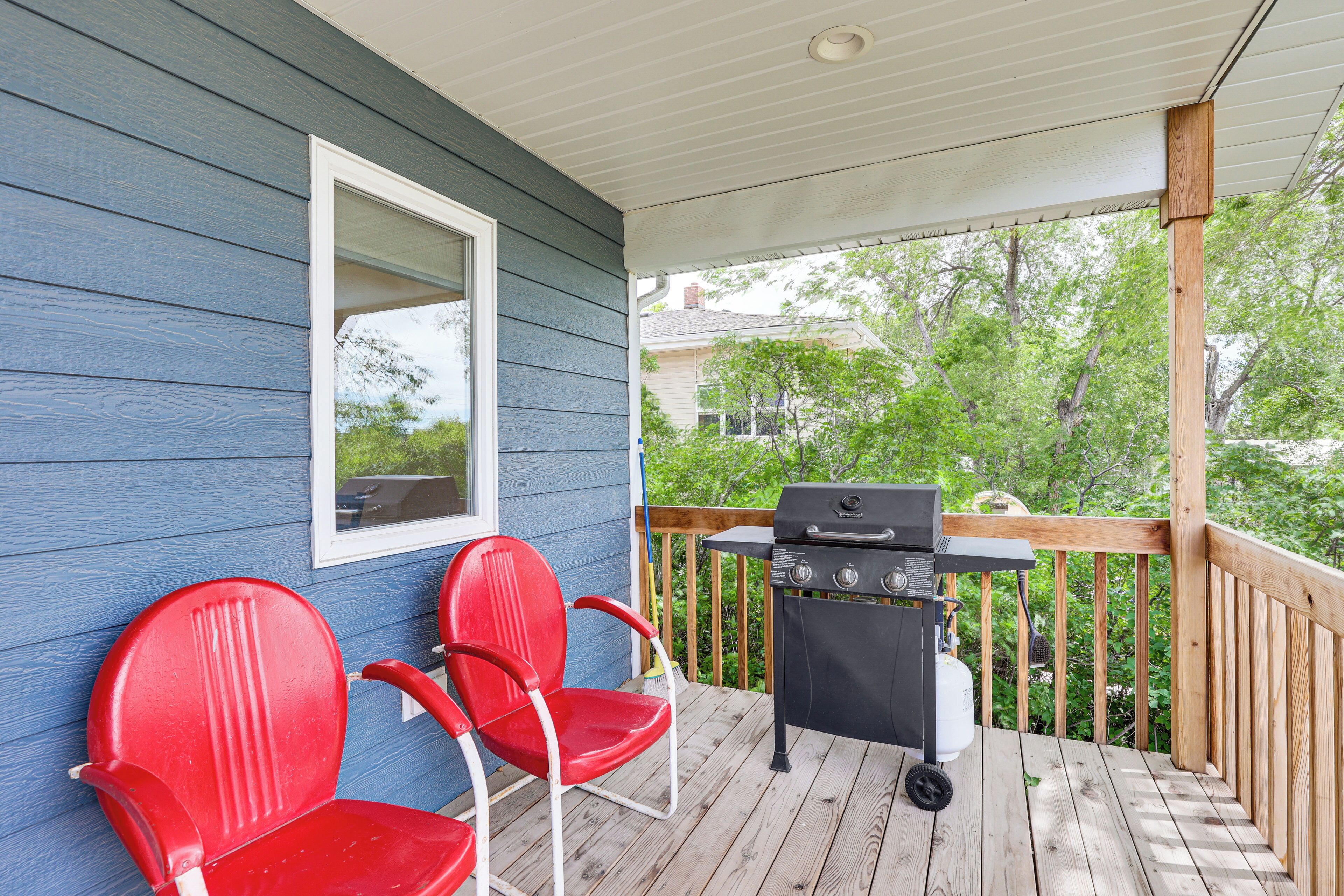 Une véranda couverte avec un barbecue et deux chaises rouges.
