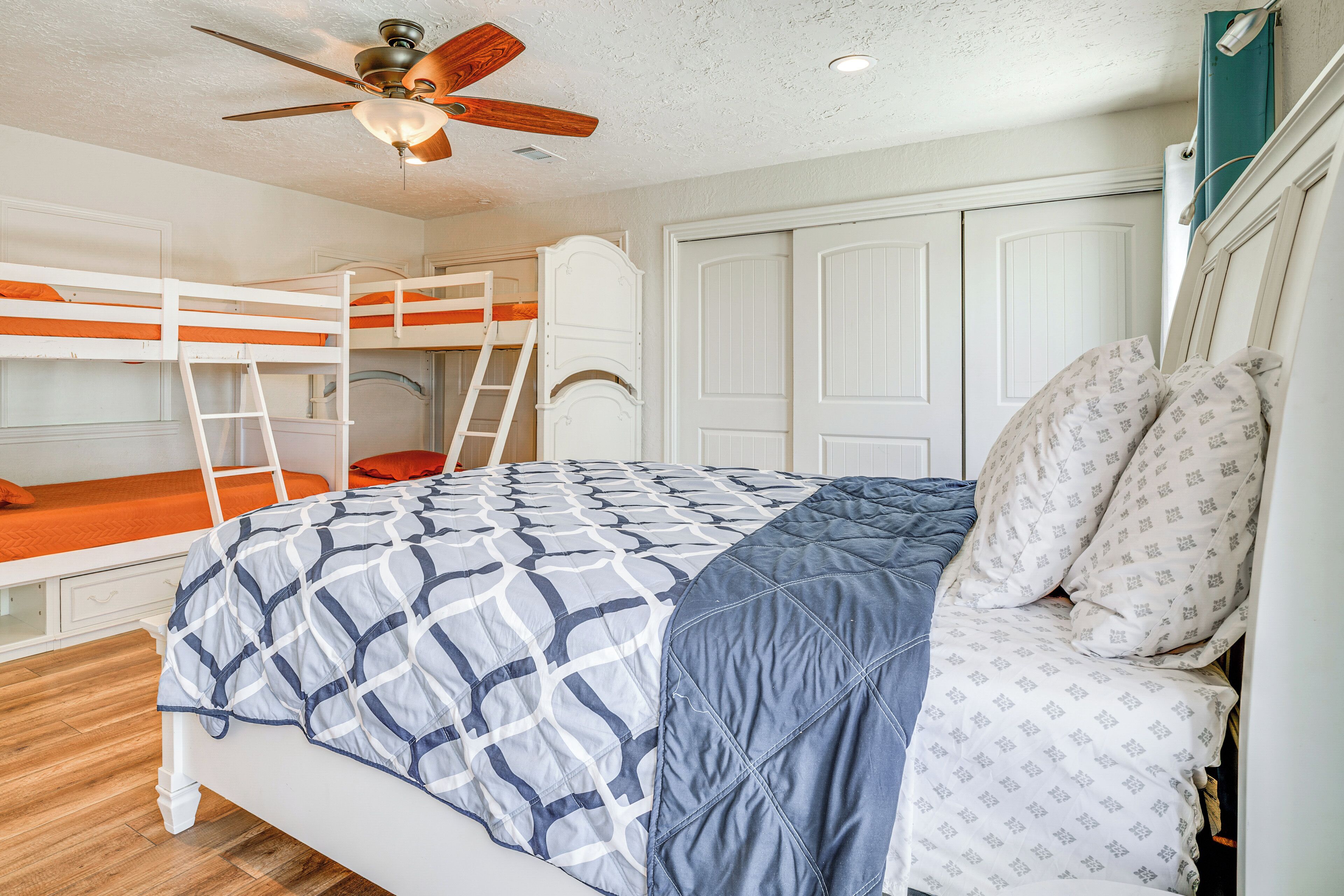 A bunk bed room with a ceiling fan, white walls, and a wooden floor.